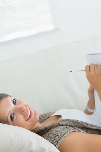 Mujer acostada en el sofá escribiendo y sonriendo —  Fotos de Stock