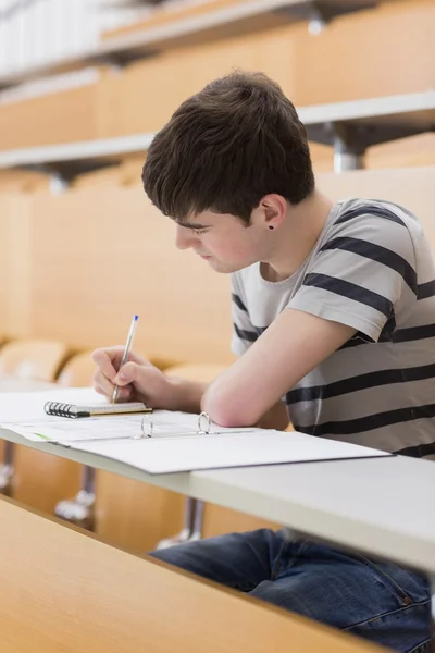 Estudante concentrado sentado enquanto escreve — Fotografia de Stock