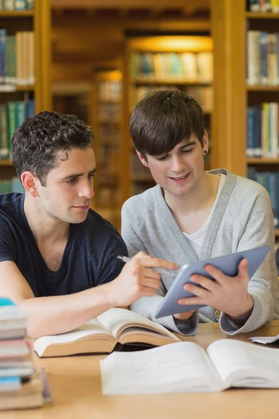 Student showing another something on tablet in library — Stock Photo, Image