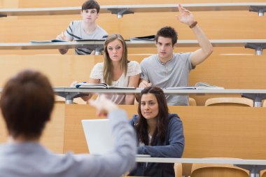 Students sitting at the lecture hall with man razing hand to ask clipart
