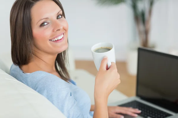 Bruna usando il suo computer portatile e bevendo una tazza di caffè — Foto Stock