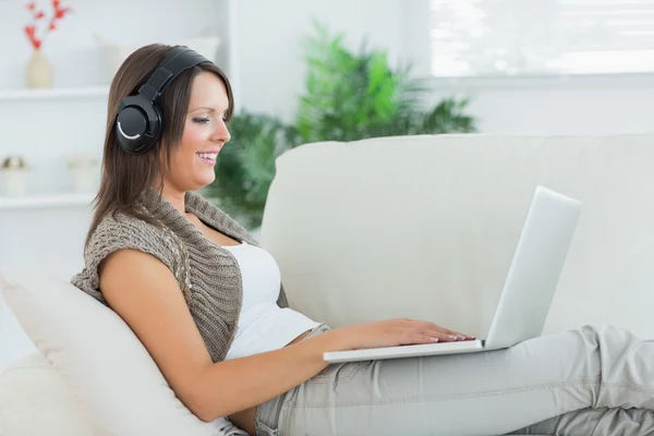 Donna felice ascoltare musica con il suo computer portatile e sdraiato sul divano — Foto Stock