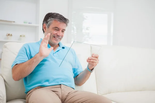 Smiling man waving at clear pane acting as digital tablet pc — Stock Photo, Image