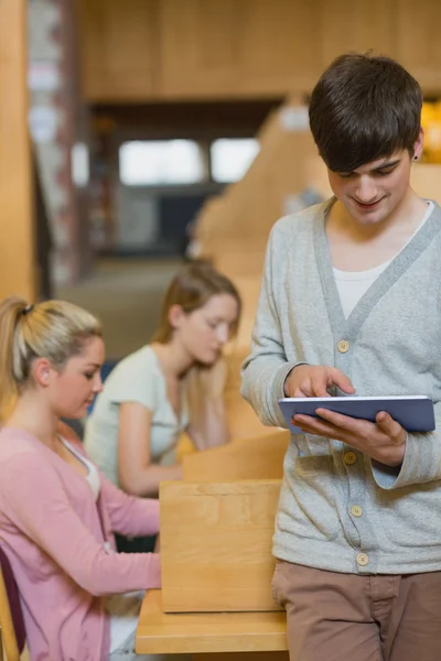 Mann steht in der Bibliothek und hält lächelnd einen Tablet-PC in der Hand — Stockfoto