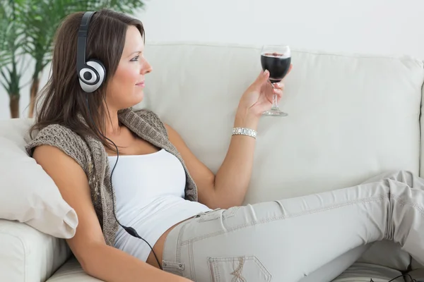 Mujer acostada en el sofá y escuchando música con un vino tinto g —  Fotos de Stock