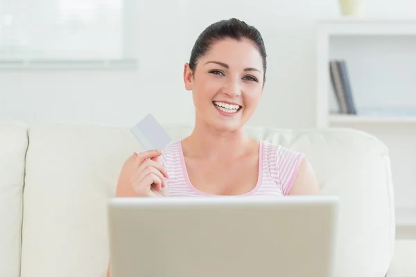 Leende kvinna använder en bärbar dator och hålla ett kreditkort — Stockfoto