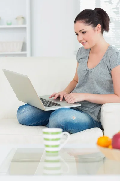 Mulher sorridente usando um laptop no sofá — Fotografia de Stock