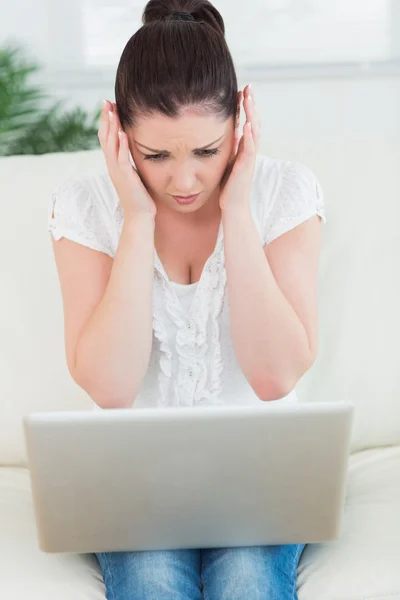 Mulher oprimida no sofá usando um laptop — Fotografia de Stock