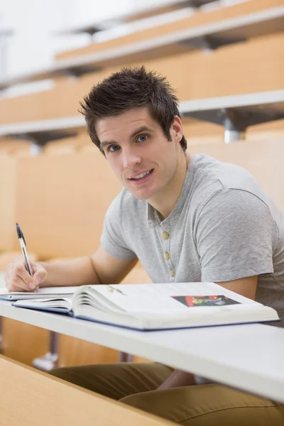 Estudante sorrindo enquanto está sentado e tomando notas — Fotografia de Stock