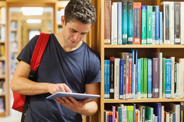 Estudiante apoyado en la estantería que sostiene una tableta pc — Foto de Stock