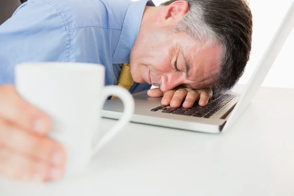 Man sleeping on his laptop while holding coffee — Stock Photo, Image