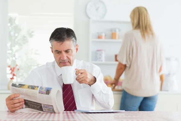 Человек, сидящий за кухонным столом во время чтения газеты — стоковое фото