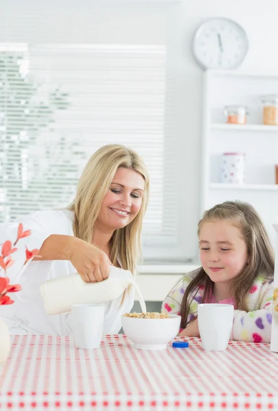 Mother pouring milk into cereal bowl for daughter — Stock Photo, Image