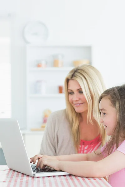 Woman and little girl sitting at the kitchen with laptop — Stock Photo, Image