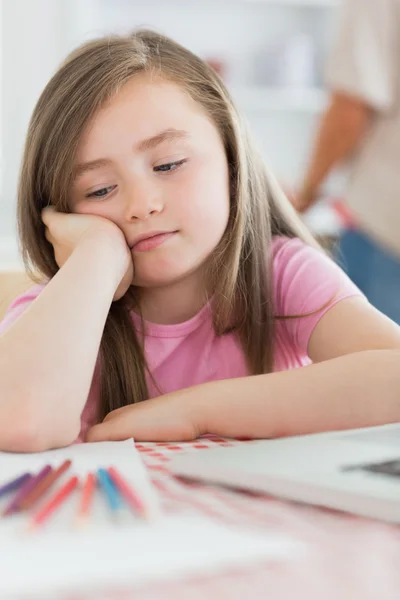 Girl sitting looking bored with paper and colouring pencils — Stock Photo, Image