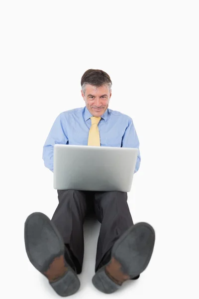 Homem sorridente escrevendo em seu laptop no chão — Fotografia de Stock