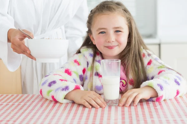 Feliz niña con un vaso de leche recibiendo cereales de su mot —  Fotos de Stock