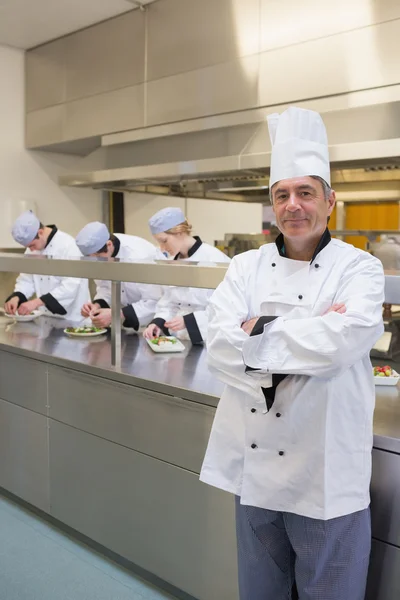 Head chef smiling with his team working behind him — Stock Photo, Image