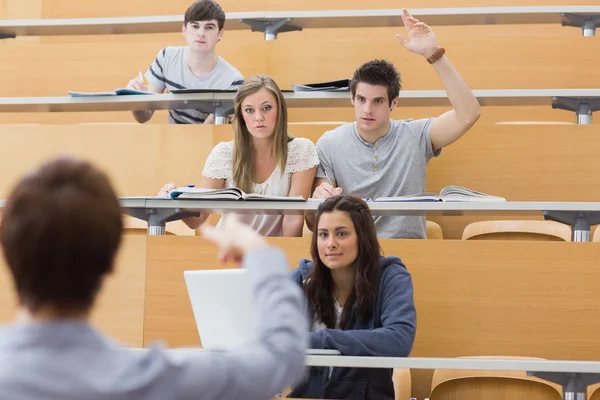 Students sitting at the lecture hall with man razing hand to ask Stock Picture