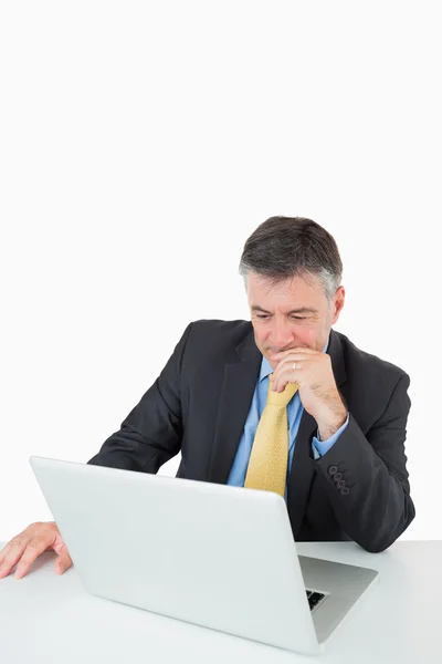 Nachdenklicher Mann sitzt mit Laptop am Schreibtisch — Stockfoto