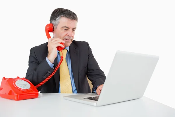 Hombre serio llamando mientras escribe en el ordenador portátil — Foto de Stock