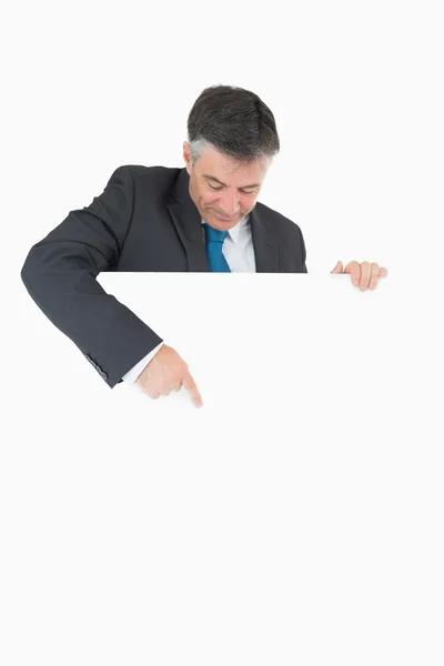 Man looking and pointing to white board he is holding — Stock Photo, Image