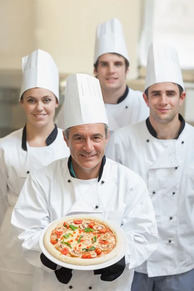 Chef presentando pizza con otros detrás de él —  Fotos de Stock