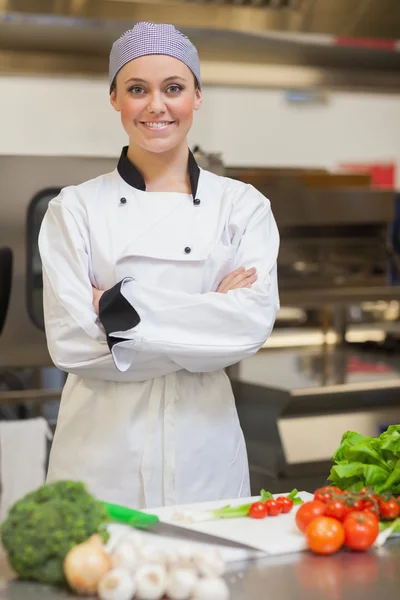 Smiling chef folding her arms beside vegetables — Stock Photo, Image