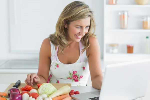 Mujer usando el ordenador portátil mientras prepara verduras —  Fotos de Stock