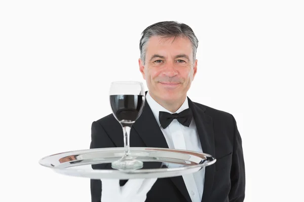 Smiling waiter holding a glass of wine on a silver tray — Stock Photo, Image