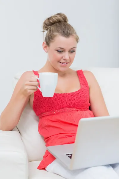 Kvinna dricker kaffe medan du använder laptop — Stockfoto