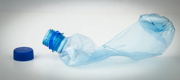 Пустая пластиковая бутылка дробленая и синий колпачок — стоковое фото