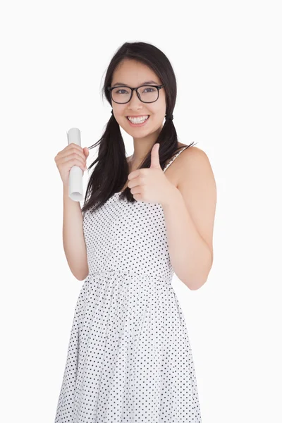 Woman giving thumbs up and holding rolled up piece of paper — Stock Photo, Image