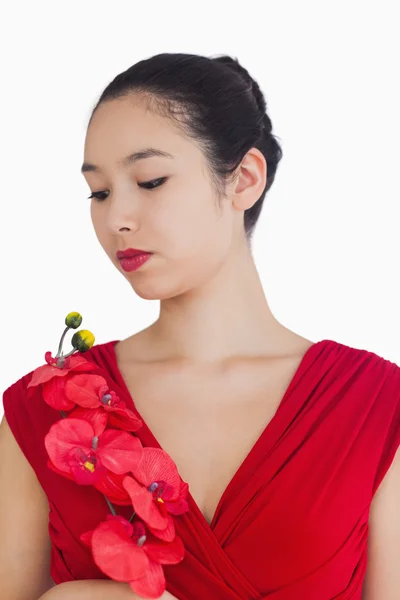 Mulher usando um vestido vermelho segurando uma orquídea vermelha — Fotografia de Stock