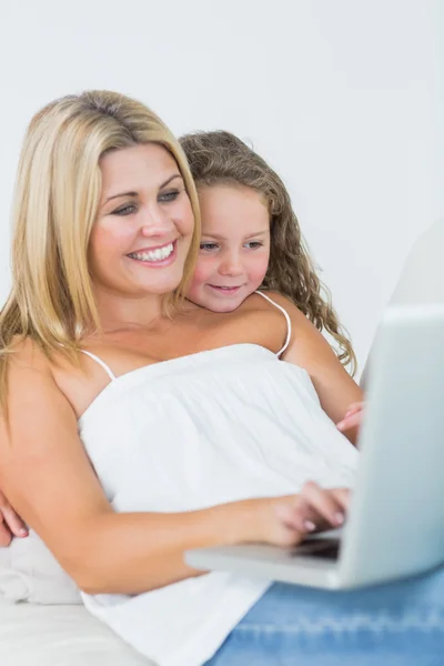Mãe usando laptop com sua filha se apoiando em seu ombro — Fotografia de Stock