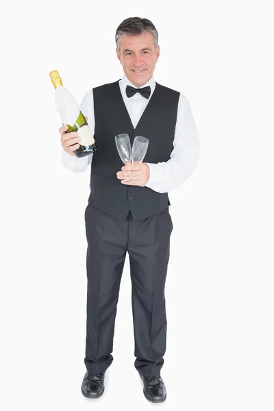 Camarero sonriente sosteniendo copas y botella de champán — Foto de Stock