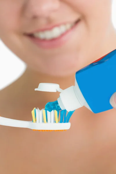 Smiling woman putting toothpaste on toothbrush — Stock Photo, Image