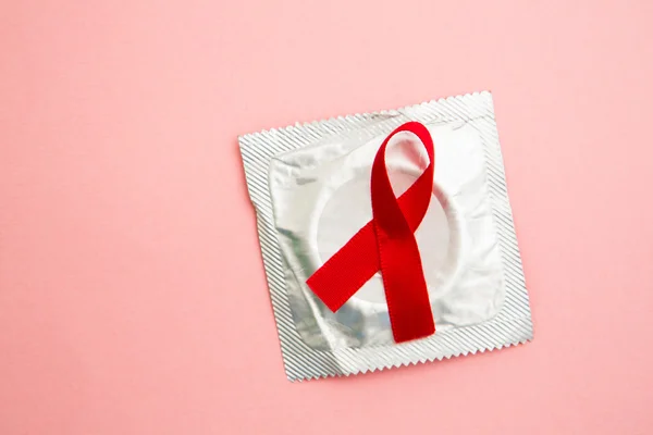 Red awareness ribbon lying on condom in wrapper — Stock Photo, Image