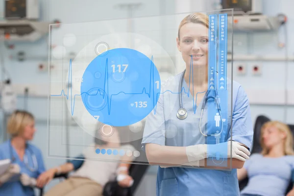Улыбающаяся медсестра, стоящая за синим экраном ЭКГ — стоковое фото