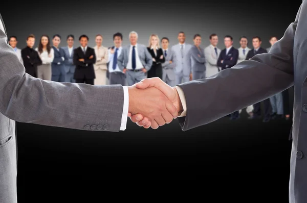 Businessmen shaking hands with large team behind them — Stock Photo, Image