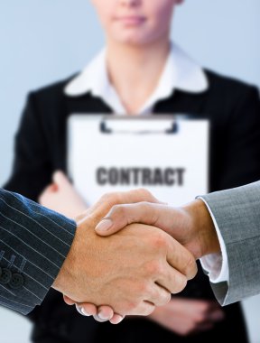 Businessmen shaking hands with contract behind them clipart
