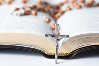 Cross of rosary beads resting against bible clipart