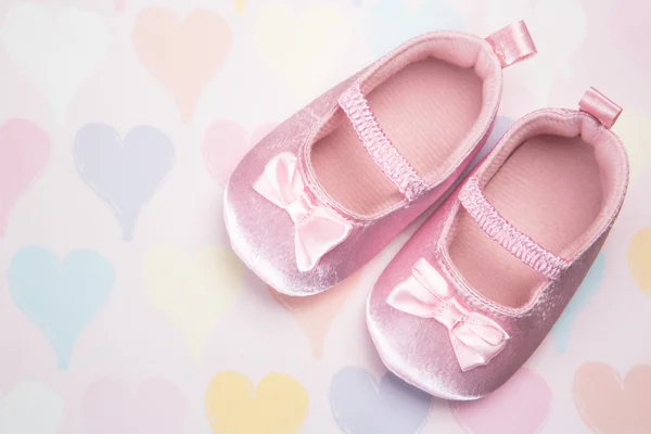 Baby pink booties on heart pattern background — Stock Photo, Image