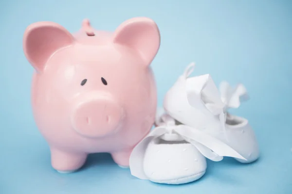 Sparschwein und weiße Babyschuhe — Stockfoto