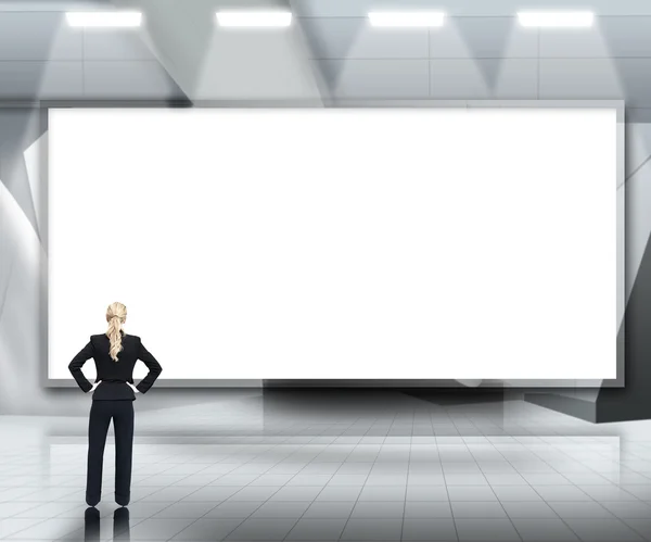 Geschäftsfrau blickt auf großen leeren Bildschirm unter Lichtern — Stockfoto