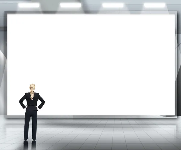 Geschäftsfrau blickt im Scheinwerferlicht auf großen leeren Bildschirm — Stockfoto