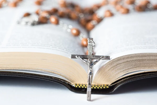 Cross of rosary beads resting against bible — Stock Photo, Image