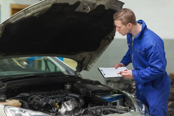 Mecánico con portapapeles examinando el motor del coche —  Fotos de Stock