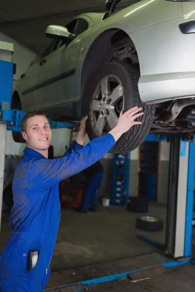 Car on hydraulic lift as mechanic examining tire — Stock Photo, Image