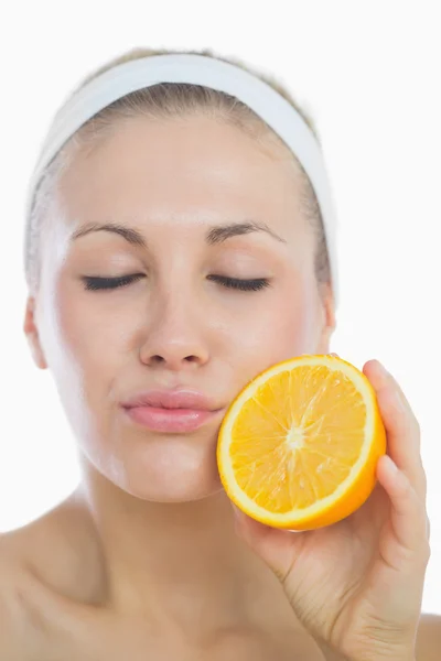 Mujer joven con los ojos cerrados sosteniendo rebanada naranja — Foto de Stock